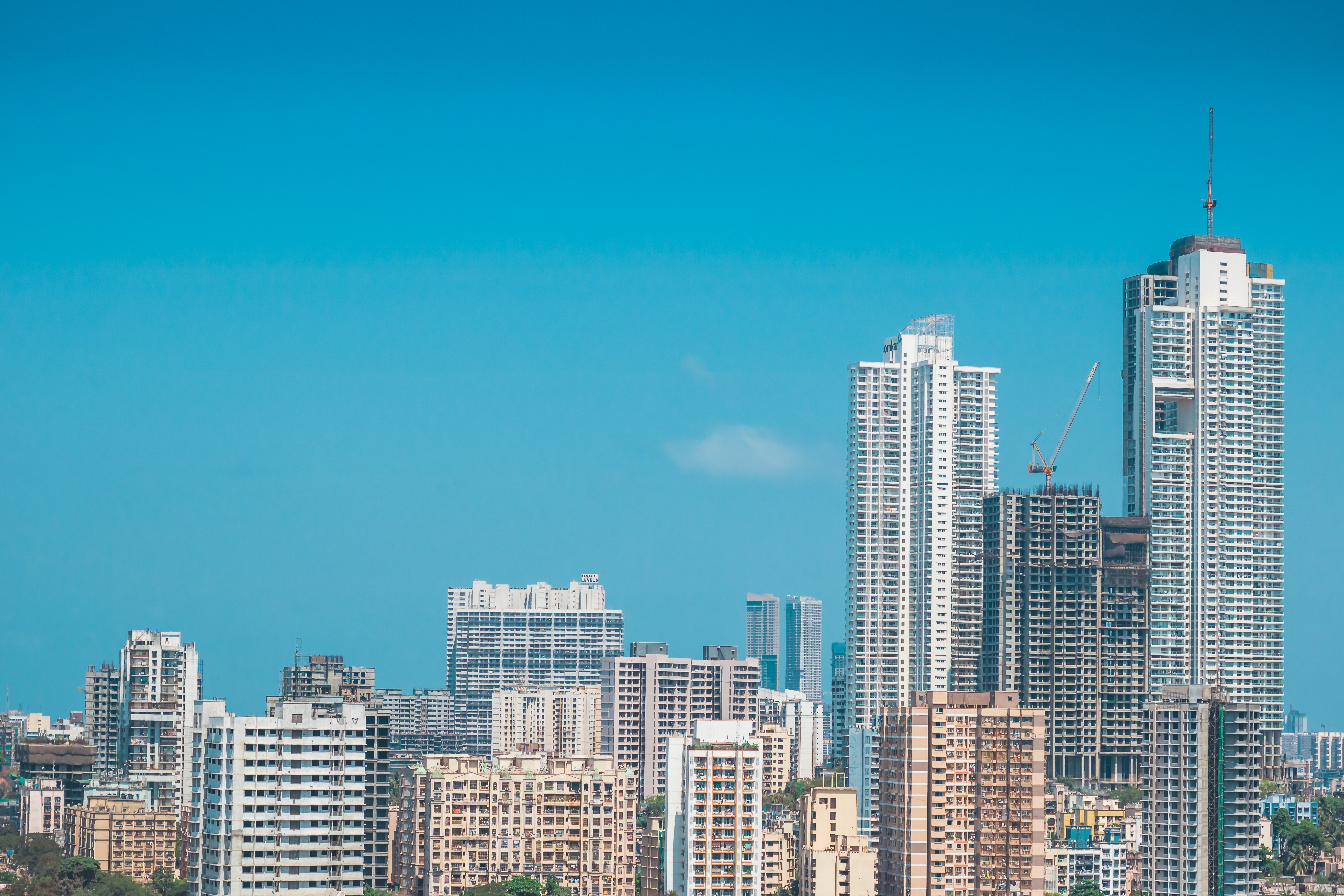 A dense Indian city skyline of high-rise buildings under a blue sky
