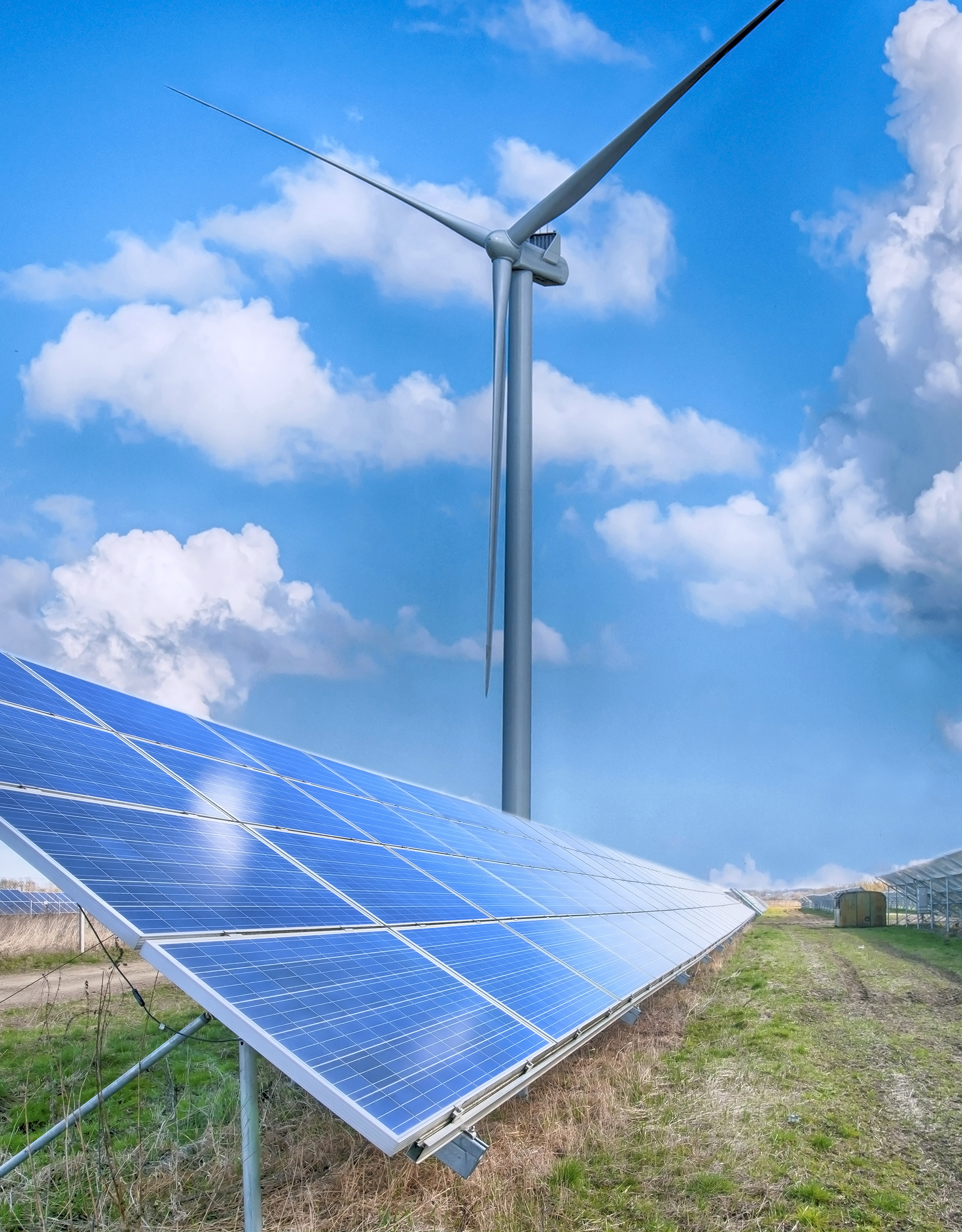 Solar panels and a wind turbine in a green field under a blue sky