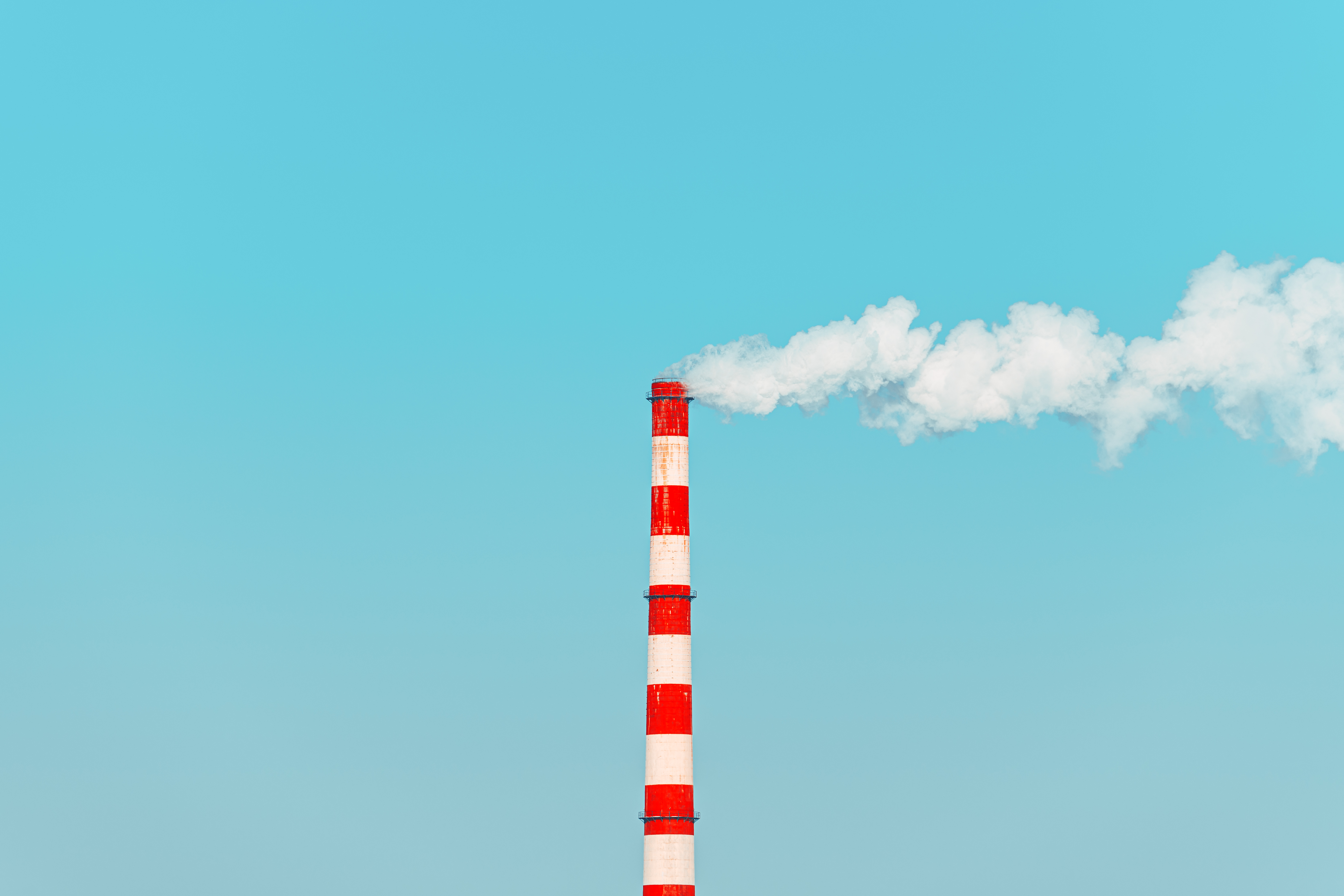 A tall red and white industrial smokestack against a clear blue sky