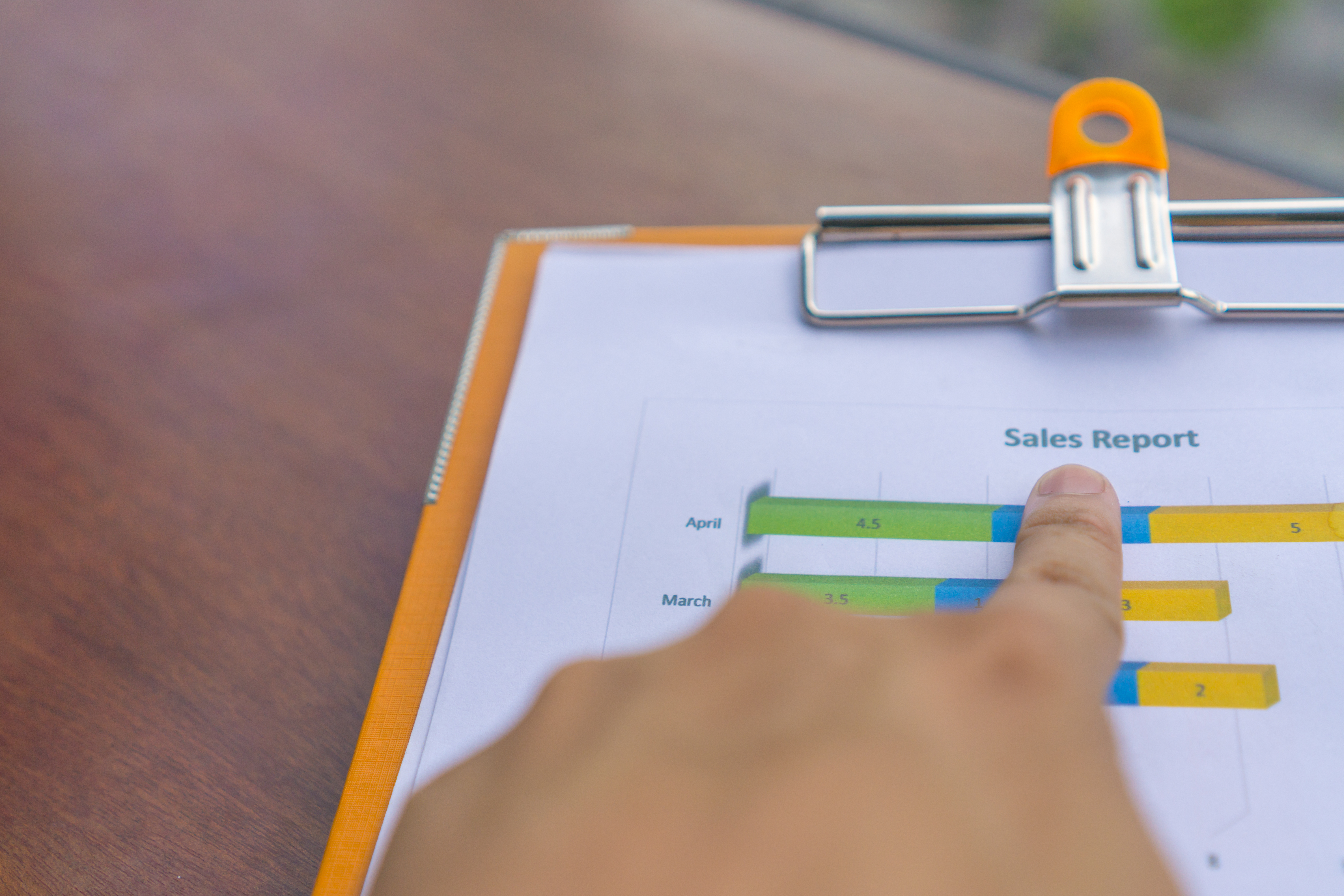 A hand pointing at a sales/data report on a clipboard