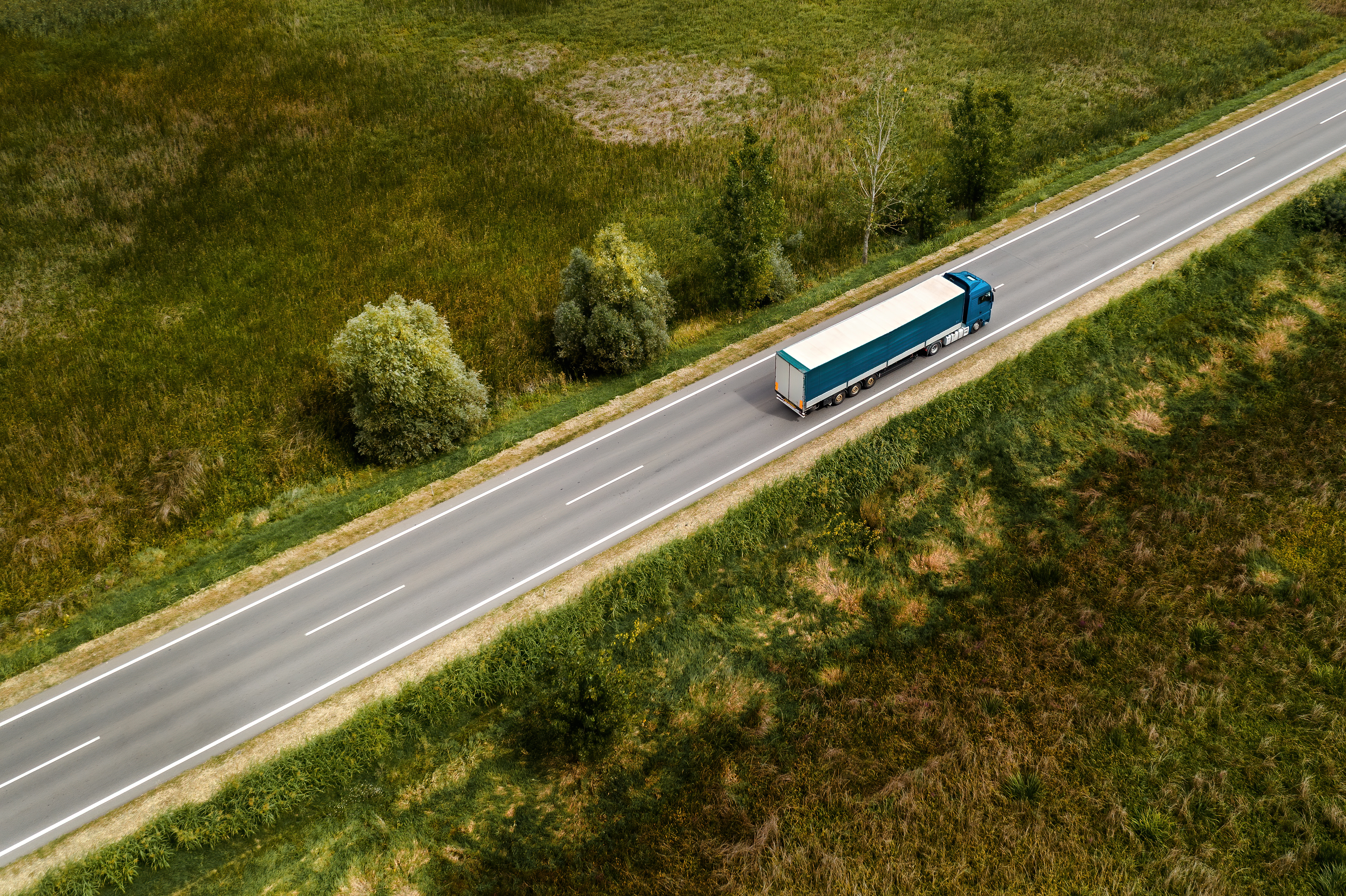 Aerial view of a freight truck driving on a highway through green countryside