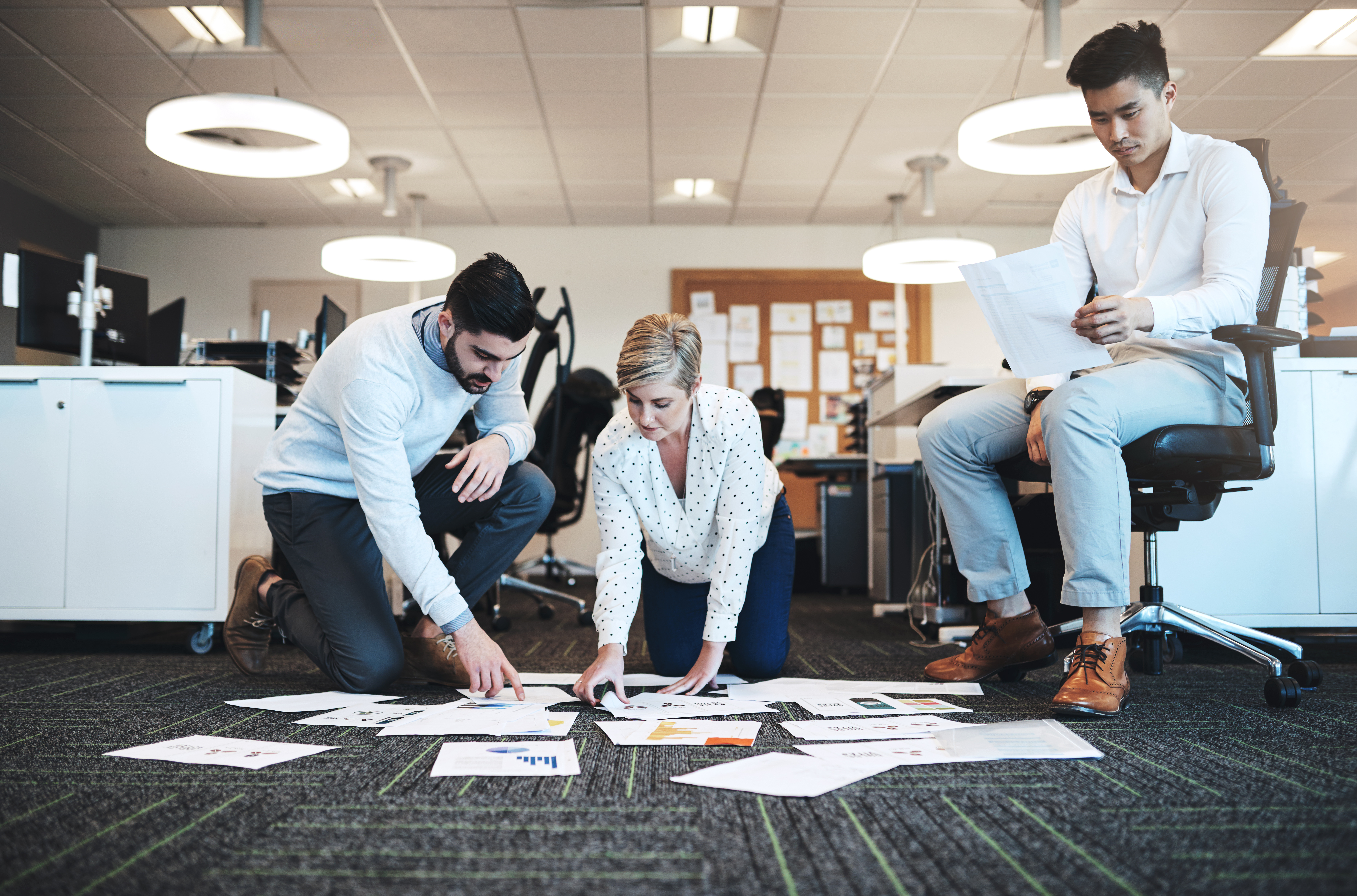 A business team reviewing data reports spread out on the office floor