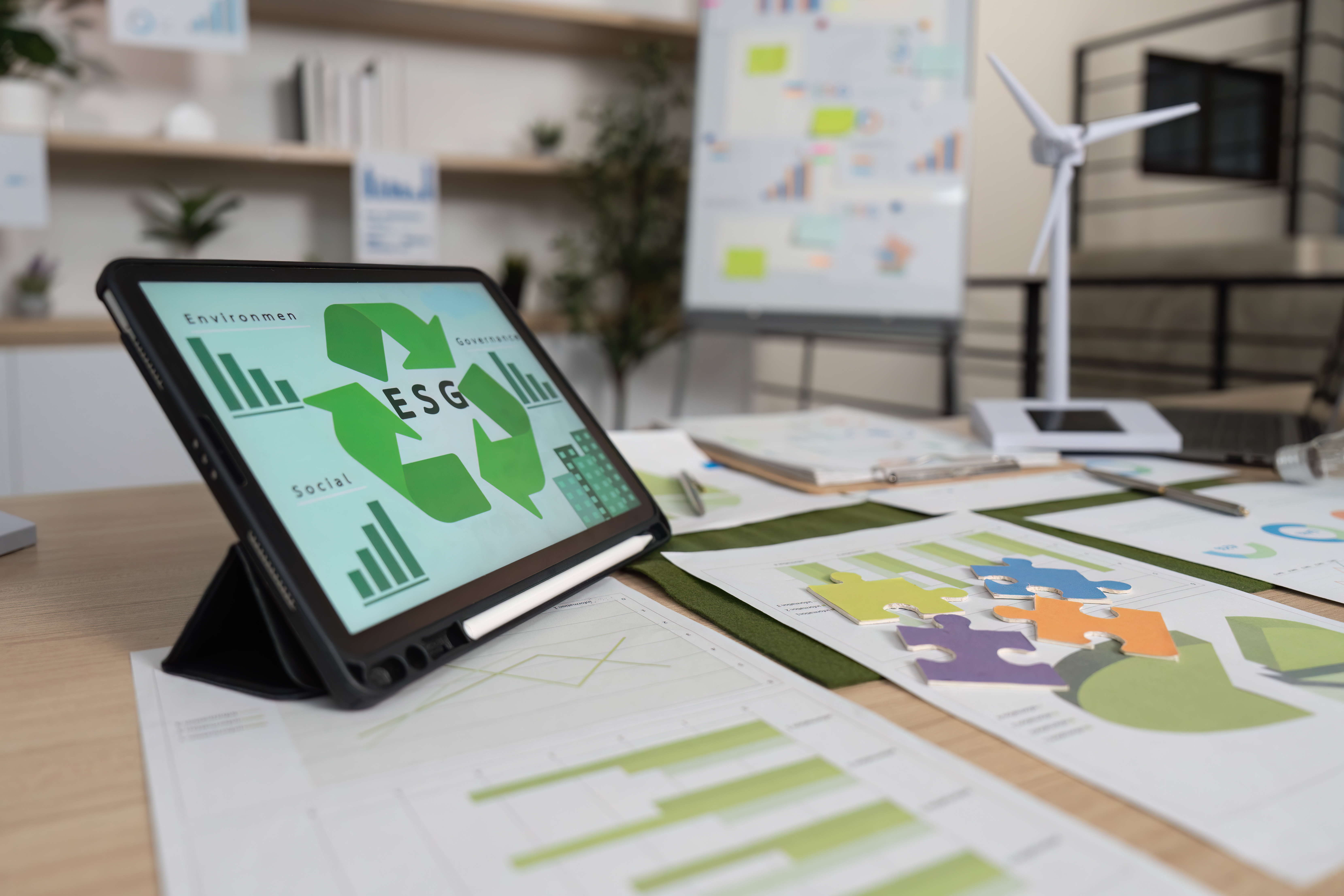 A tablet displaying "ESG" with environmental, social, and governance icons on an office desk