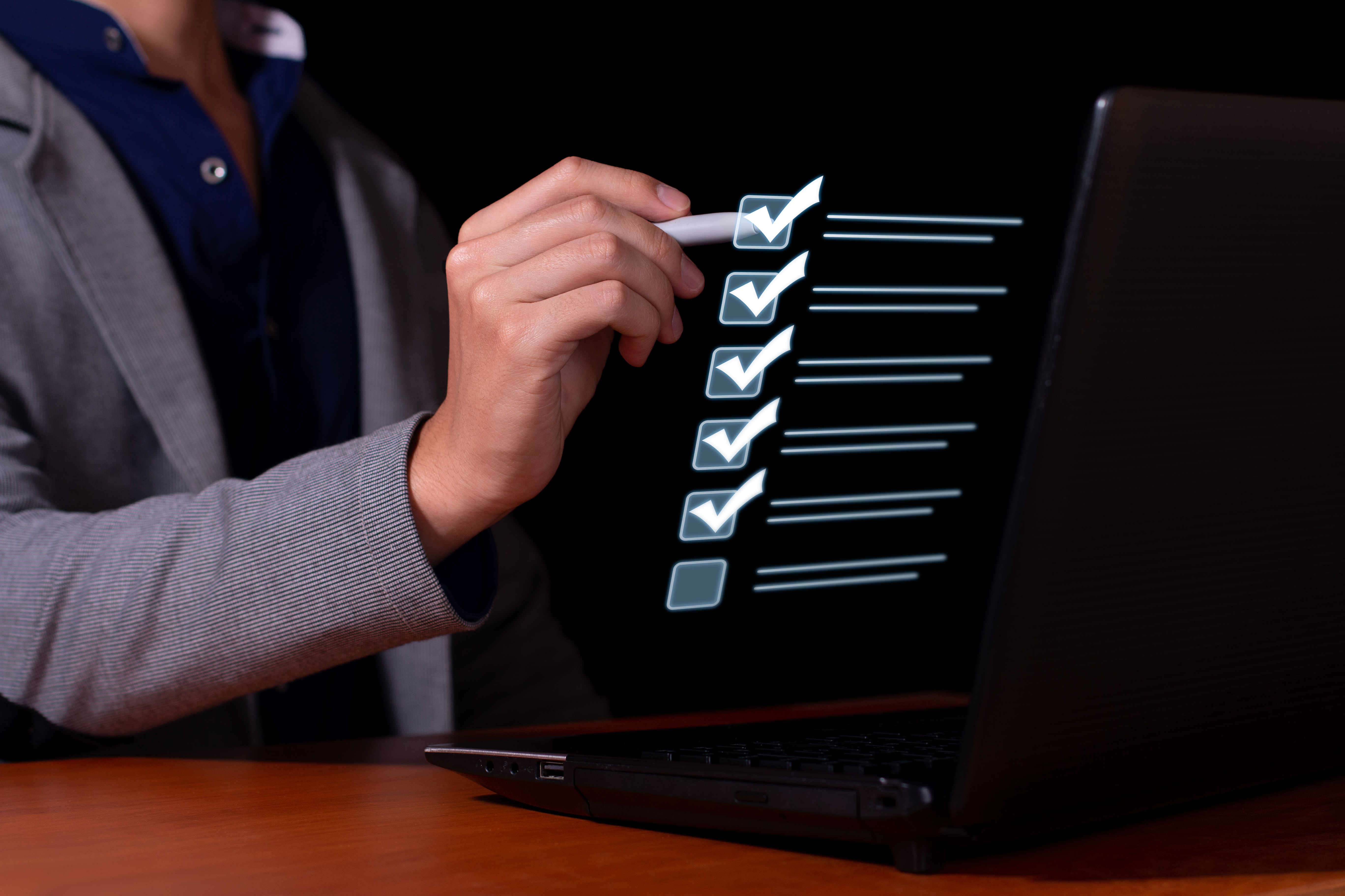 A businessman checking off items on a glowing virtual checklist above a laptop